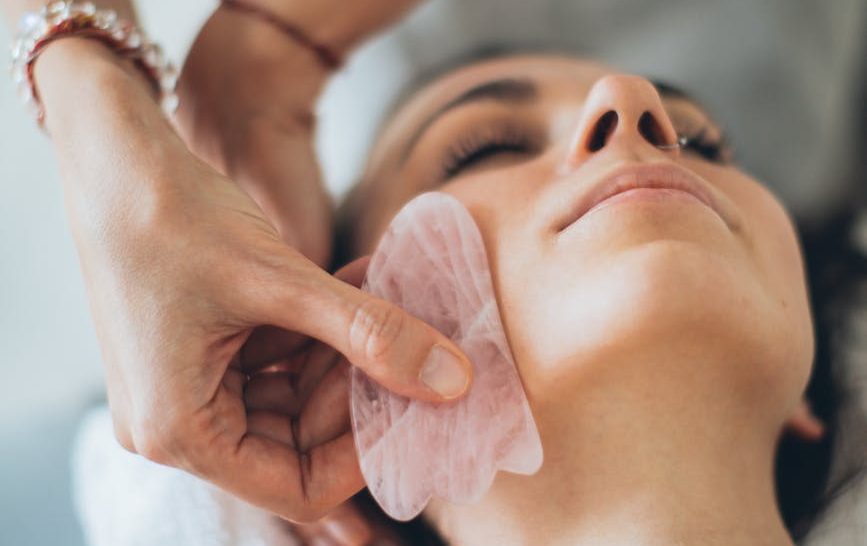 a person touching a woman s face using gua sha